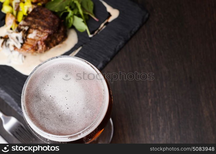 Beer glass and steak. Beer glass and steak on black table, view from above.