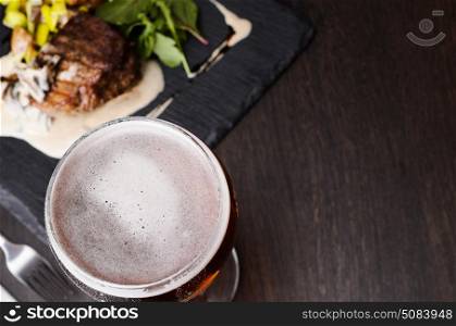 Beer glass and steak. Beer glass and steak on black table, view from above.