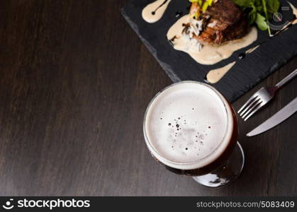 Beer glass and steak on black table, view from above.