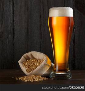 Beer glass with bag full of beer barley for brewing, on wooden table with copy space