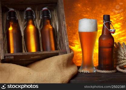 Beer glass with wooden crate full of beer bottles and wheat ears on table