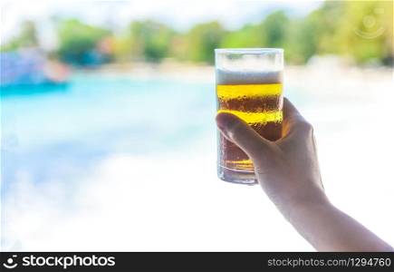 Beer mug in hand with sea background / hand holding a mug of beer on beach in summer hot weather ocean landscape nature outdoor vacation