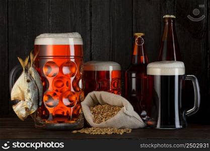 Beer mugs and bottles assortment with smoked salty fish, barley bag, dark wooden background with copy space