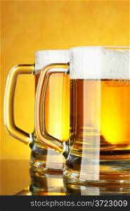 Beer mugs with froth over yellow background