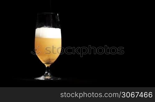 Beer pours in glass on black.