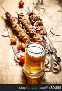 Beer with pork Shish kebab and tomatoes. On a wooden table.. Beer with pork Shish kebab and tomatoes.