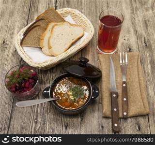 Beet salad and tomato, red pepper soup, sauce with olive oil, rosemary and smoked paprika with fork and a glass of juice and knife on a wooden background.