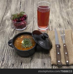 Beet salad and tomato, red pepper soup, sauce with olive oil, rosemary and smoked paprika with fork and a glass of juice and knife on a wooden background.
