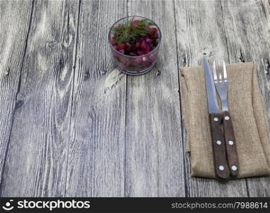 Beet salad salad in a glass vase with fork and knife on a wooden background.. Beet salad salad in a glass vase with fork and knife on a wooden background
