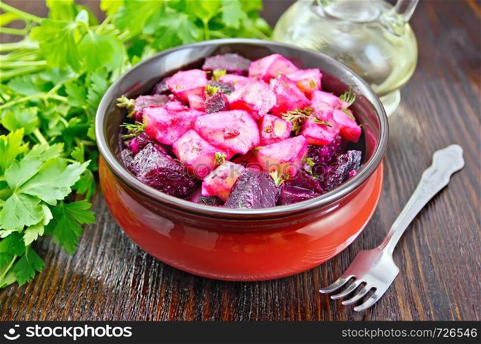 Beetroot and potato salad, seasoned with vegetable oil and vinegar in a bowl, parsley, fork against a dark wooden board