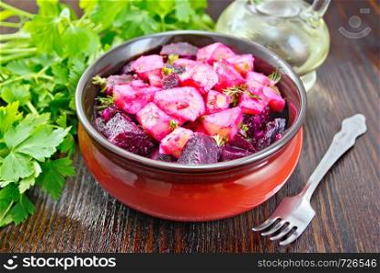 Beetroot and potato salad, seasoned with vegetable oil and vinegar in a bowl, parsley, fork against a dark wooden board