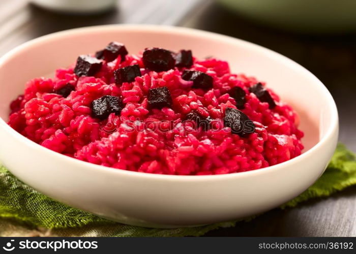 Beetroot risotto prepared with beetroot puree, roasted beetroot pieces on top, photographed with natural light (Selective Focus, Focus on the first beetroot pieces on top of the risotto)