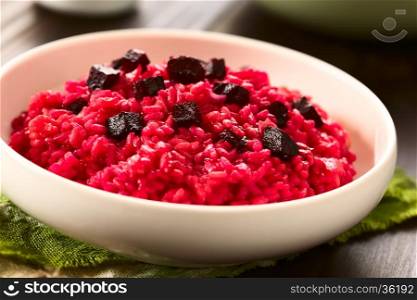 Beetroot risotto prepared with beetroot puree, roasted beetroot pieces on top, photographed with natural light (Selective Focus, Focus on the first beetroot pieces on top of the risotto)