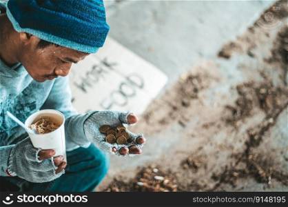 Begging under the bridge with a cup containing coins and instant noodles