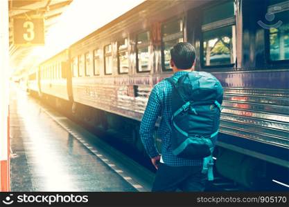 Behind asian young man standing and waiting train on platform.