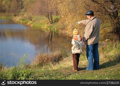 Behind grandfather with grandson in wood in autumn look on water
