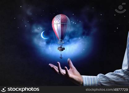 Behind the edge of your imagination. Male hand holding aerostat balloon flying in sky
