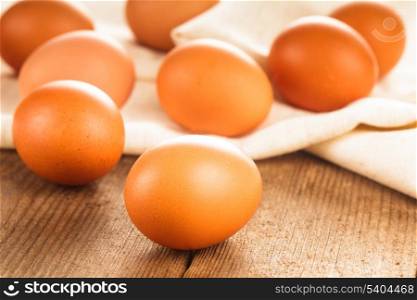 Beige chicken eggs on textile tablecloth over rustic wooden table