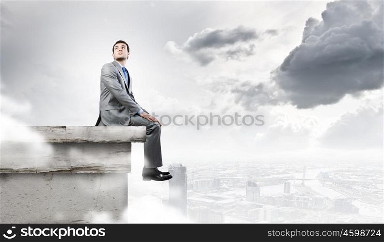 Being at the top. Young handsome businessman sitting at the edge of building roof