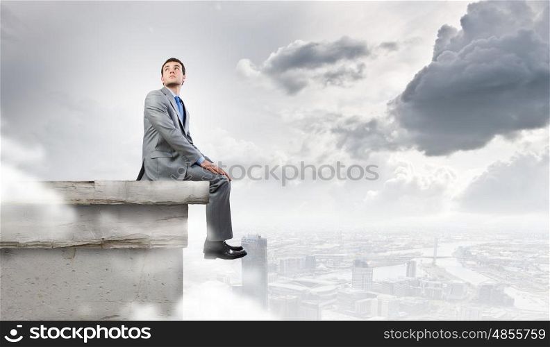 Being at the top. Young handsome businessman sitting at the edge of building roof