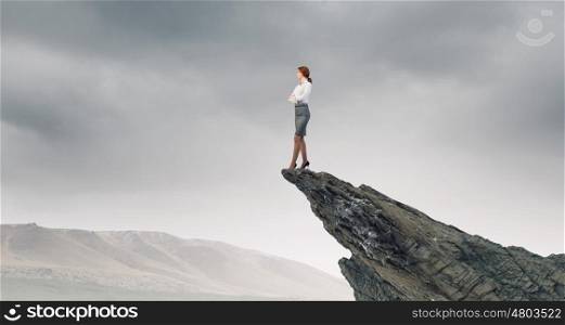 Being on top. Businesswoman with arms crossed on chest standing on edge of rock
