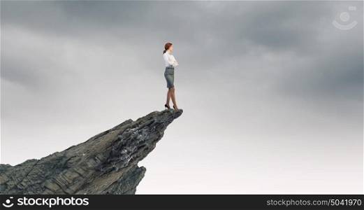 Being on top. Businesswoman with arms crossed on chest standing on edge of rock
