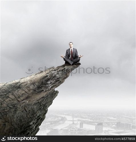 Being on top. Young businessman sitting on edge of rock