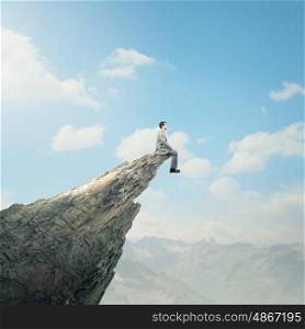 Being on top. Young businessman sitting on edge of rock