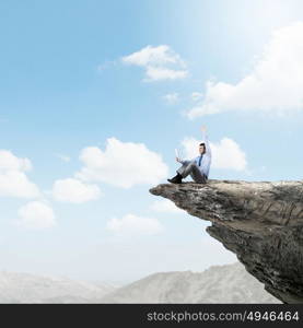 Being on top. Young businessman sitting on edge of rock