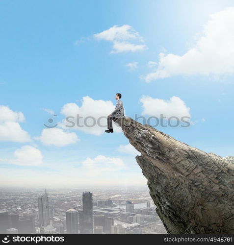 Being on top. Young businessman sitting on edge of rock