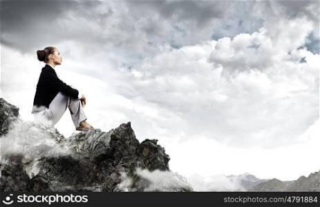 Being on top. Young pretty businesswoman sitting on top of mountain