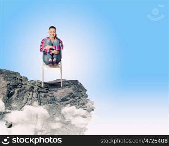 Being on top. Young woman in casual sitting in chair on top of rock