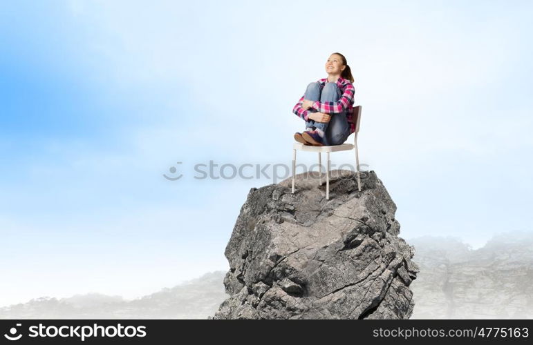 Being on top. Young woman in casual sitting in chair on top of rock