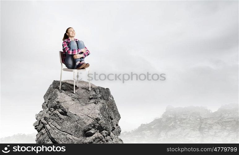 Being on top. Young woman in casual sitting in chair on top of rock