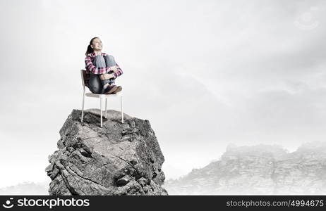 Being on top. Young woman in casual sitting in chair on top of rock