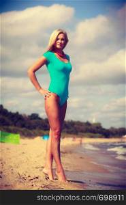 Being trendy and fashionable during summer vacation concept. Blonde slim attractive woman walking on beach wearing blue one piece swimsuit.. Woman walking on beach wearing swimsuit