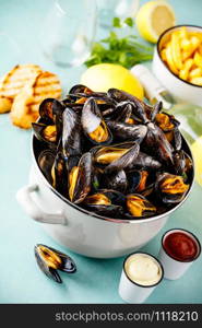 Belgian mussels in white wine with lemon, herbs, croutons and french fries on blue background