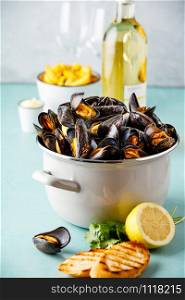 Belgian mussels in white wine with lemon, herbs, croutons and french fries on blue background