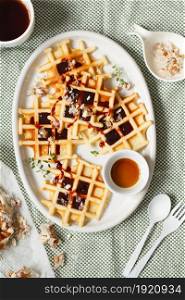 Belgian or Brussels waffles with date syrup or jam and candied roasted nuts. Homemade waffles in a white oval Plate on the kitchen table. Traditional classic Viennese waffles closeup