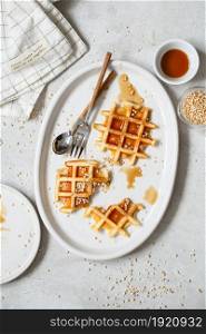 Belgian or Brussels waffles with maple syrup and puffed quinoa pops. Almost empty plate with delicious Brussels waffles eaten.