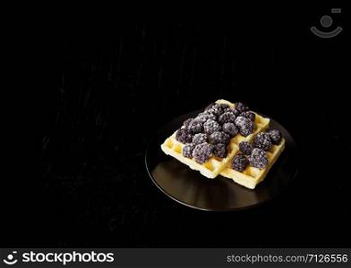 Belgian wafers with frozen blackberries on a black background.. Belgian waffles with blackberry