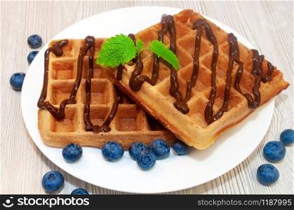 Belgian waffles on a plate with chocolate sauce and blueberries with mint. Belgian waffles on a plate with chocolate sauce and blueberries