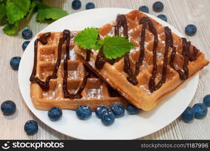 Belgian waffles on a plate with chocolate sauce and blueberries with mint. Belgian waffles on a plate with chocolate sauce and blueberries