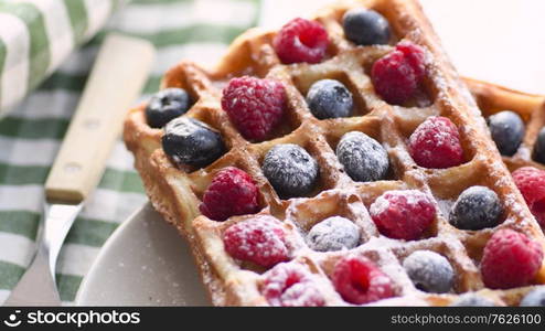 Belgian waffles on plate with berries. Sweet waffle breakfast. Dessert served on table with napkin and fork.. Belgian waffles on plate with berries