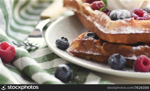 Belgian waffles on plate with ice cream and berries. Sweet waffle breakfast. Dessert served on table with napkin and fork.. Belgian waffles on plate with ice cream