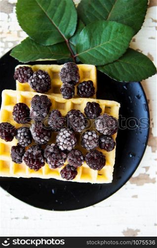 Belgian waffles with blackberries on a wooden background with green leaves.. Belgian waffles with blackberry