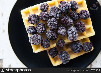 Belgian waffles with blackberries on the old wooden table, close-up.. Belgian waffles with blackberry