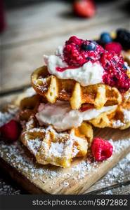 Belgian waffles with fresh berries on rustic wooden background