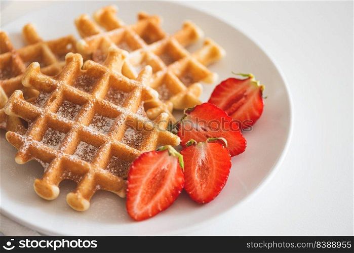 Belgian waffles with strawberry and powdered sugar on white plate. Breakfast food concept. Copy space