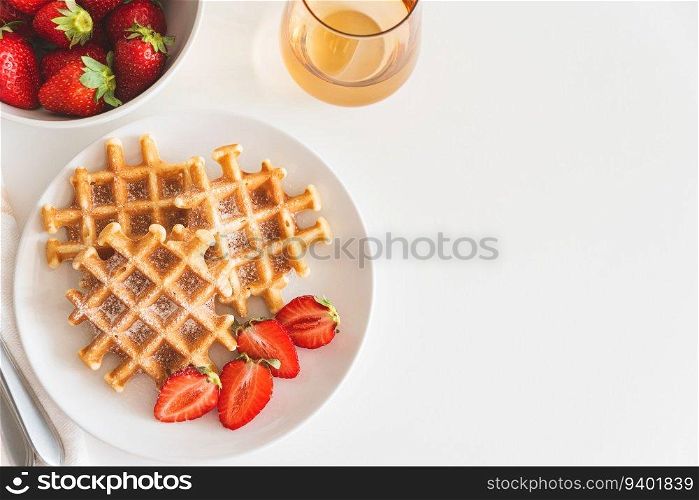 Belgian waffles with strawberry and powdered sugar on white plate. Breakfast food concept. Copy space. Top view